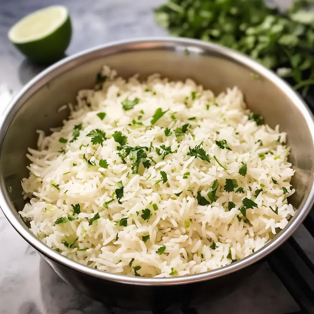 A bowl of fluffy white rice garnished with fresh cilantro, alongside a halved lime and some cilantro leaves.