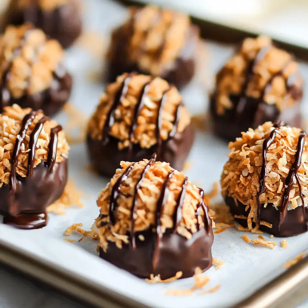 Chocolate-covered coconut treats are arranged on a parchment-lined tray, featuring a drizzle of chocolate on top.