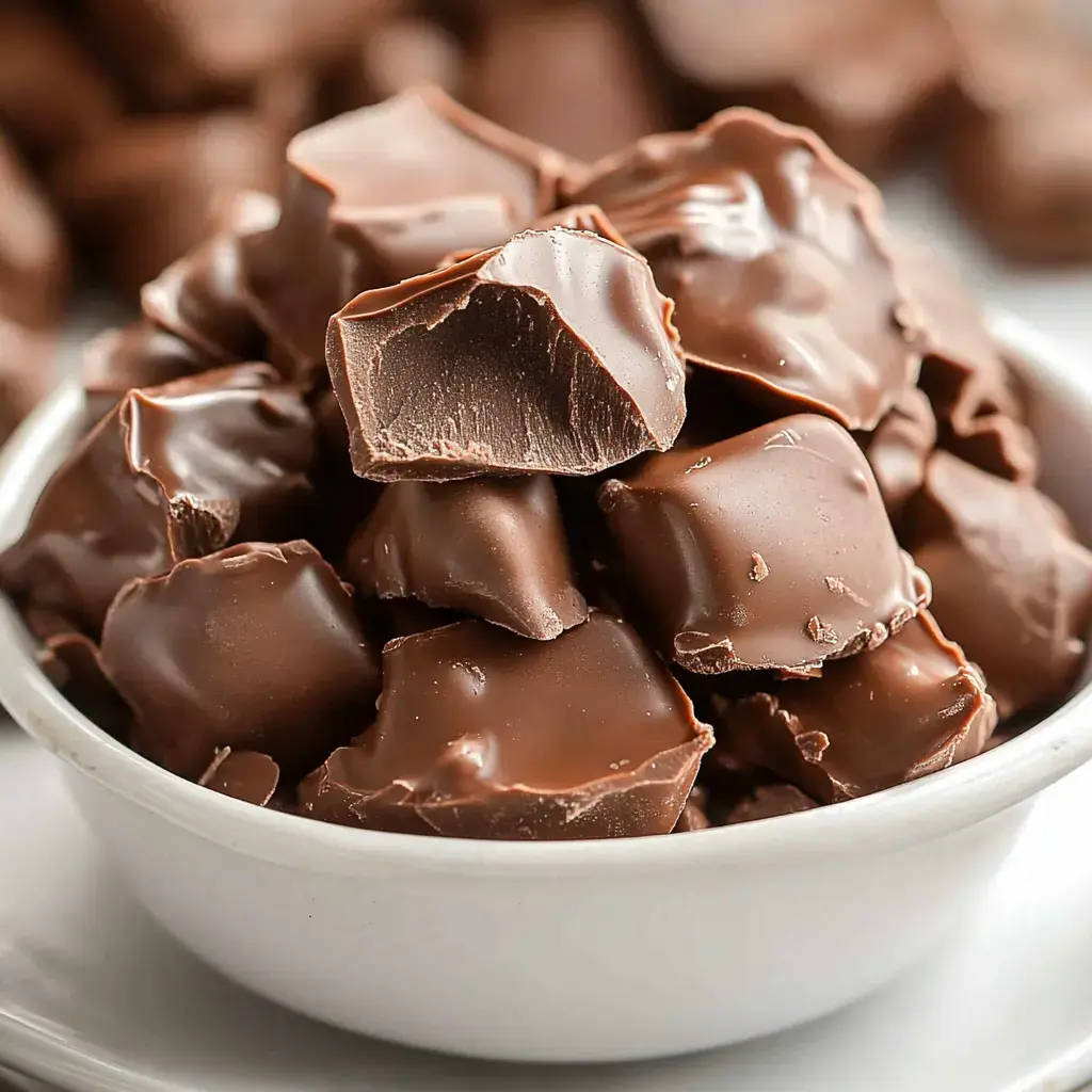 A white bowl filled with chunks of smooth chocolate, some of which are partially broken.