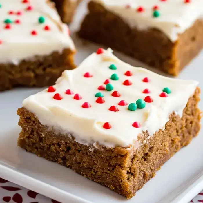 A close-up of a frosted cake square topped with red and green decorations, served on a white plate.