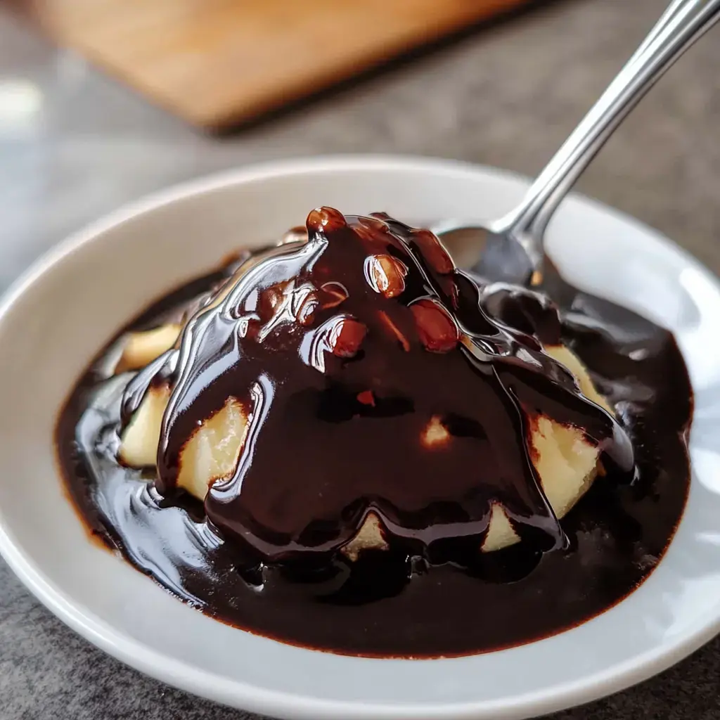 A scoop of vanilla ice cream topped with rich chocolate sauce and drizzled with nuts, served in a white bowl.