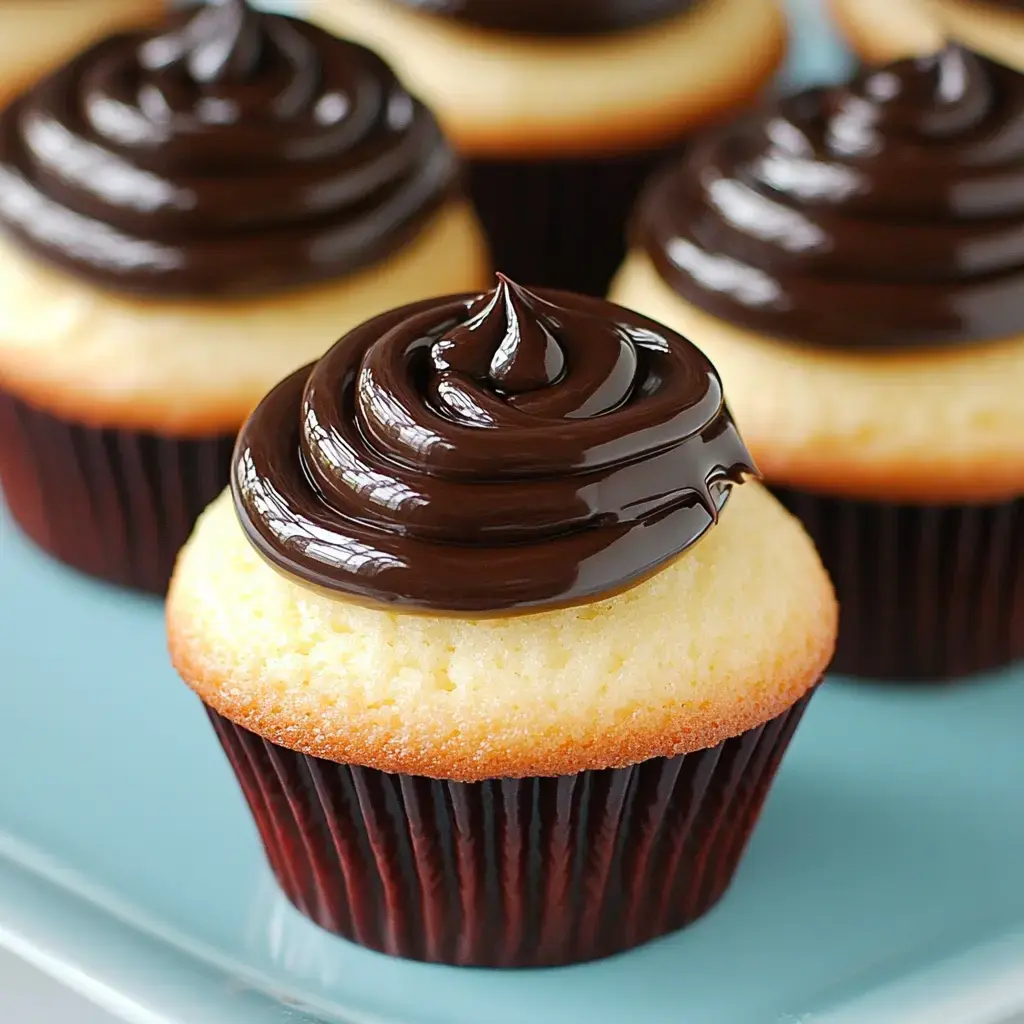 A close-up of yellow cupcakes with glossy chocolate frosting arranged on a light blue plate.