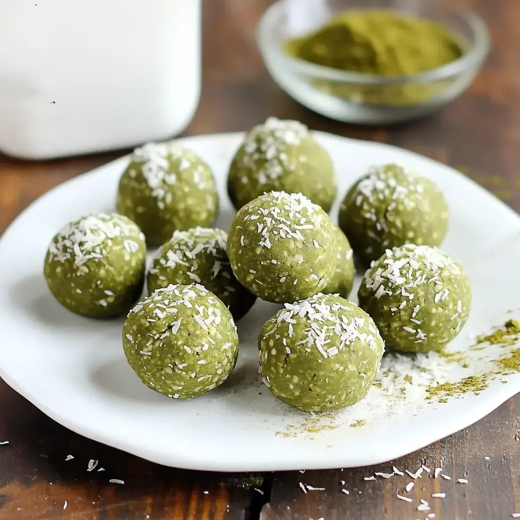 A plate of green energy balls coated with shredded coconut, garnished with a sprinkle of powdered green ingredients in the background.