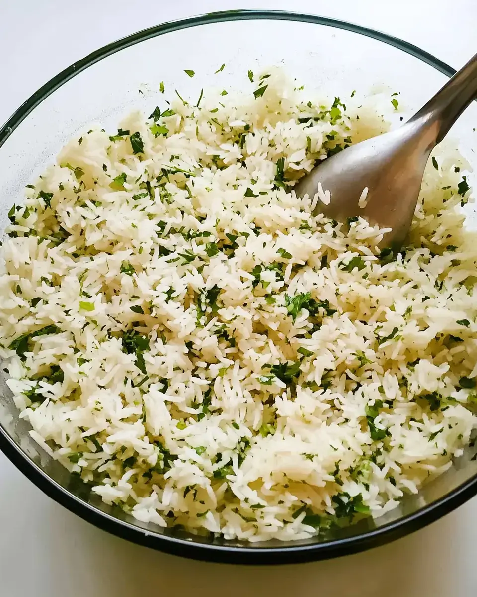 A glass bowl filled with fluffy white rice mixed with fresh chopped herbs.