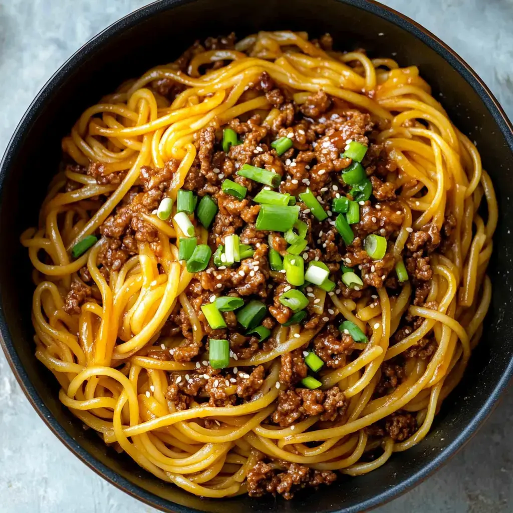 A close-up of a bowl of spaghetti topped with ground meat, green onions, and sesame seeds.