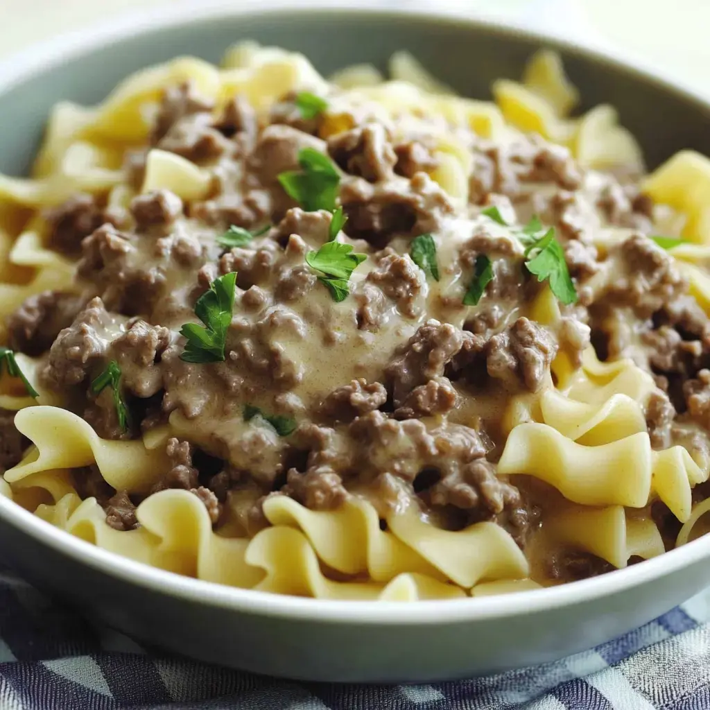 A bowl of egg noodles topped with creamy ground beef and garnished with parsley.