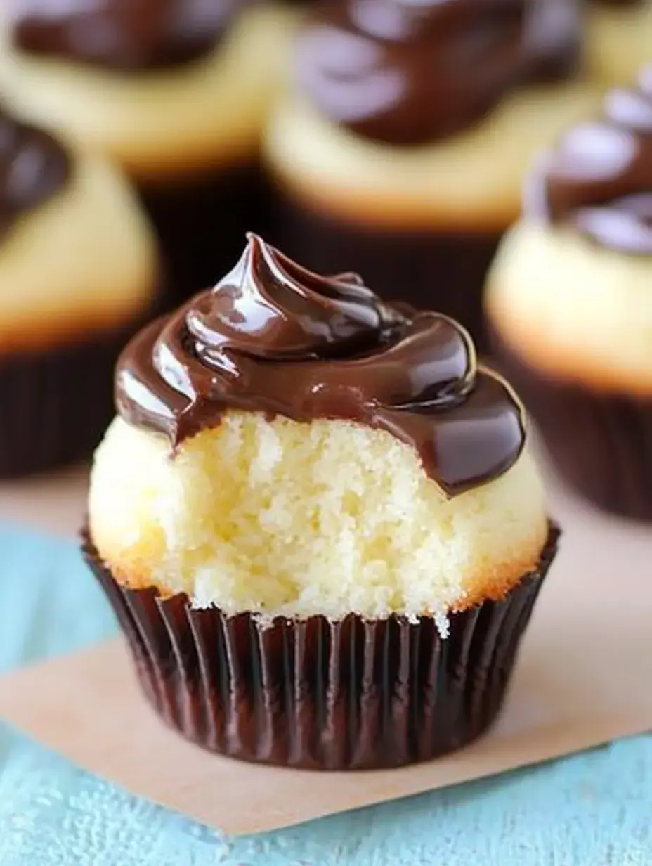 A close-up of a partially eaten vanilla cupcake topped with rich chocolate frosting, with other cupcakes slightly blurred in the background.