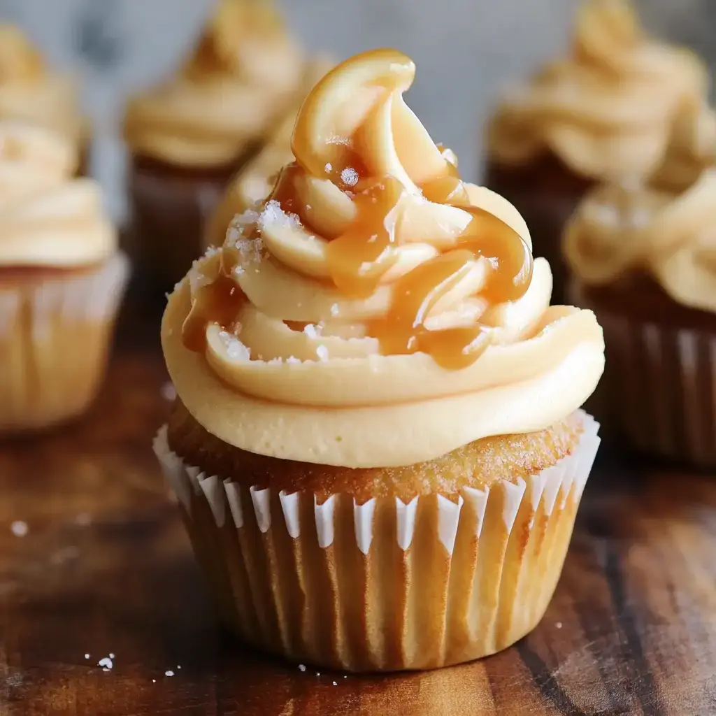 A close-up of a vanilla cupcake topped with creamy caramel frosting and a drizzle of caramel sauce.