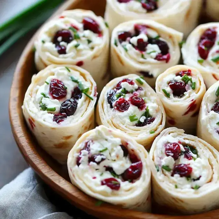 A wooden bowl filled with sliced pinwheel wraps containing cream cheese, cranberries, and chives.