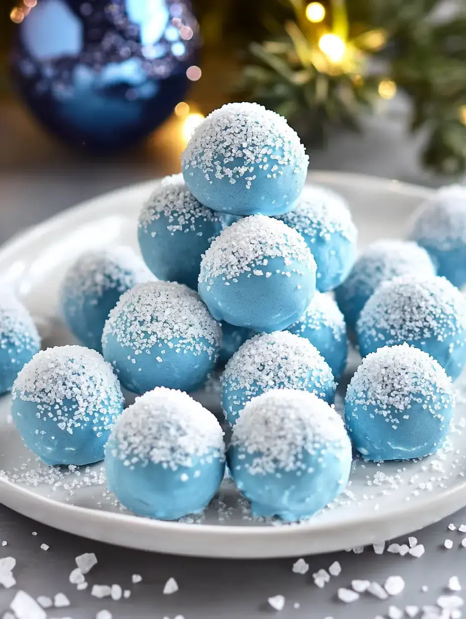 A plate of decorative blue dessert balls, topped with white sugar crystals, is arranged in a snowy style, with festive decorations in the background.