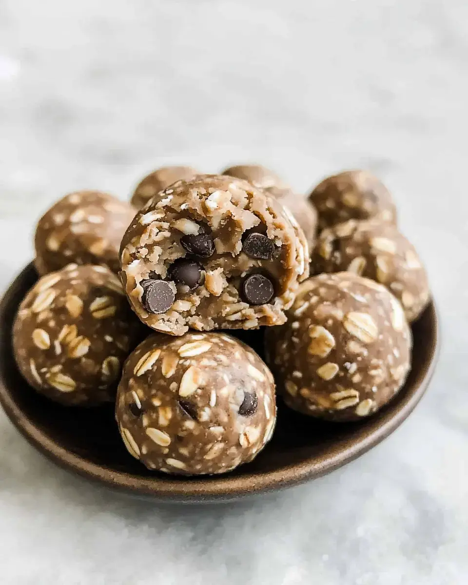 A close-up of a bowl filled with energy balls made of oats, nuts, and chocolate chips, with one ball cut in half to reveal its interior.