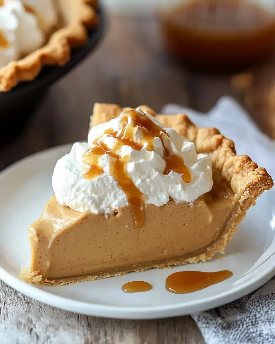 A slice of creamy pumpkin pie topped with whipped cream and caramel drizzle on a white plate.