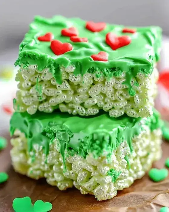 A close-up of two stacked green rice crispy treats decorated with red heart shapes on top.