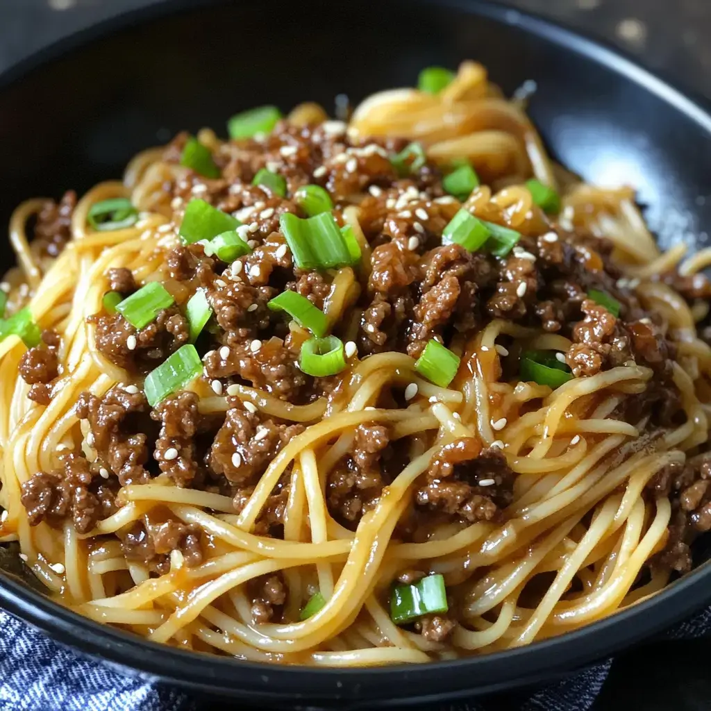 A close-up of a bowl of noodles topped with seasoned ground beef, green onions, and sesame seeds.