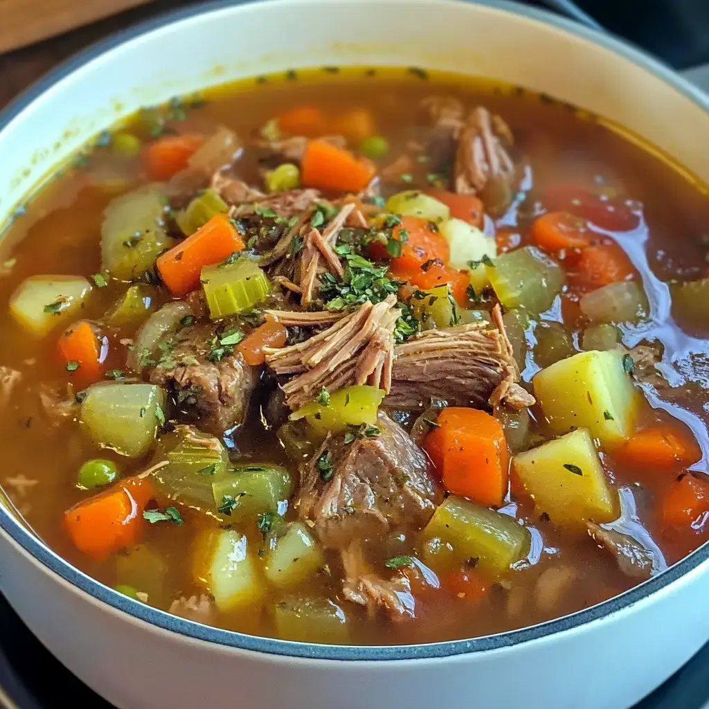 A hearty bowl of beef vegetable soup featuring chunks of tender meat, carrots, celery, and peas in a savory broth.