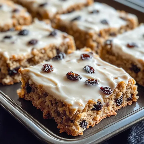 A pan of cake with white icing and raisins.