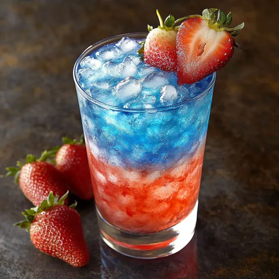 A glass of blue, red and white drink with strawberries on the side.