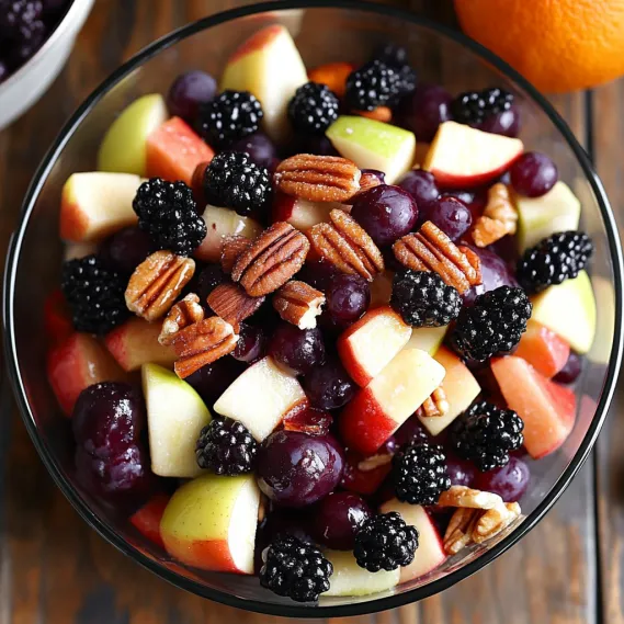 A bowl of fruit with blackberries, apples, oranges, and blueberries.