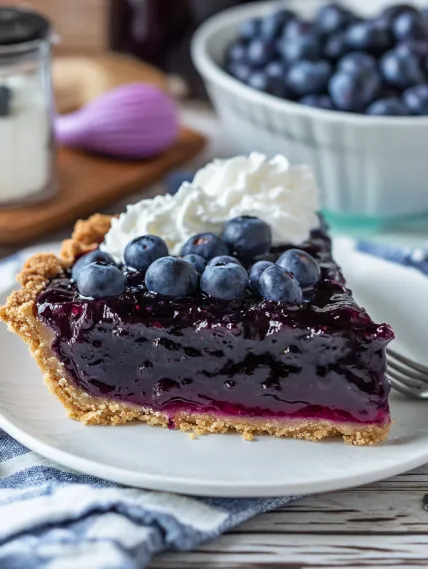 A slice of blueberry pie with whipped cream on top.