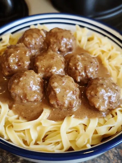 A bowl of pasta with meatballs and gravy.