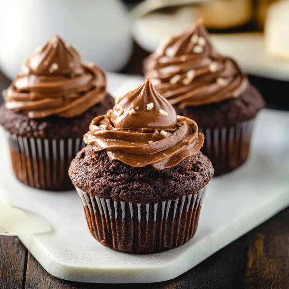 Three chocolate cupcakes with white frosting and chocolate sprinkles.