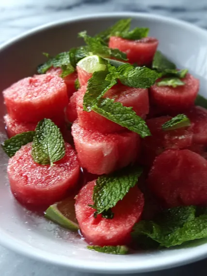 A bowl of watermelon slices with mint leaves.