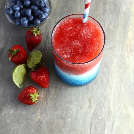 A glass of red, white and blue drink with strawberries and blueberries.