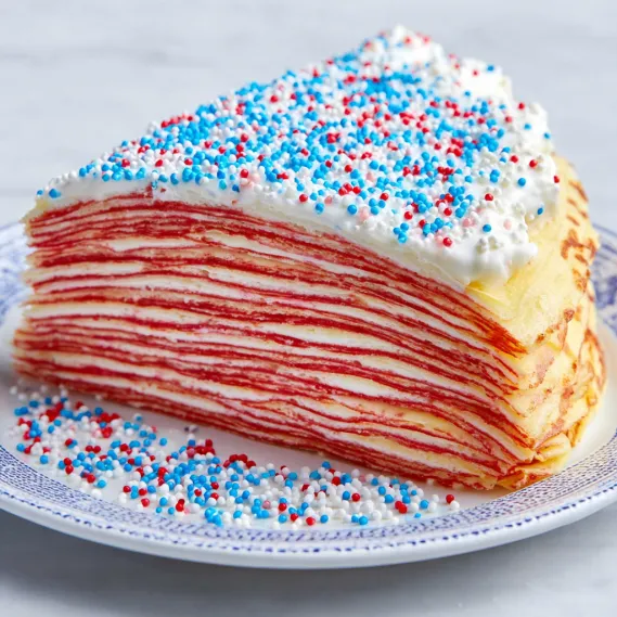 A slice of red velvet cake with white frosting and blue sprinkles.