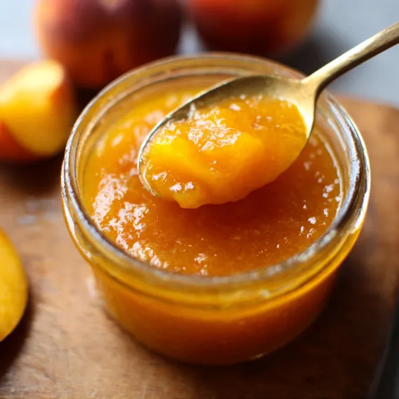 A jar of peach jam with a spoon in it.