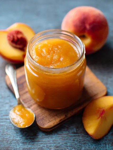 A jar of peach jam on a wooden block.