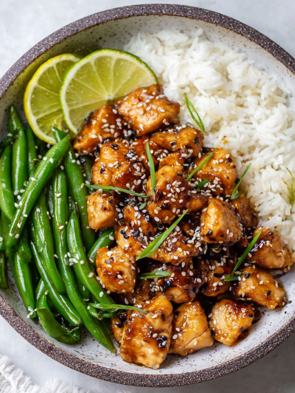 A bowl of healthy sesame chicken with rice and green beans.