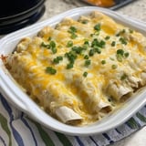 A baked dish of cheese-covered enchiladas garnished with chopped green onions, served in a white casserole dish.