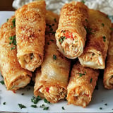 A close-up of crispy fried rolls filled with a savory chicken mixture, garnished with parsley on a white plate.