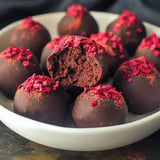 A plate of chocolate truffles topped with red raspberry bits, with one truffle cut in half to reveal a moist chocolate center.