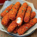 A plate of crispy, orange-coated cheese sticks, one partially bitten to reveal the gooey cheese inside, garnished with herbs.