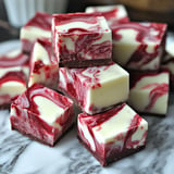 A close-up of beautifully swirled red and white fudge cubes stacked on a marble surface.