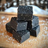 A stack of chocolate squares topped with black sprinkles on a wooden surface, surrounded by scattered salt crystals.