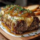 A succulent meatloaf topped with melted cheese, caramelized onions, and fresh parsley, served on a wooden cutting board with slices of bread in the background.