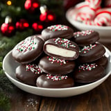 A plate of chocolate-covered cookies with festive sprinkles, featuring one cookie cut in half to reveal a creamy filling.