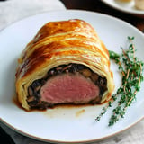 A beautifully plated beef Wellington, showcasing a golden-brown pastry exterior and a cross-section revealing tender pink beef surrounded by mushrooms.