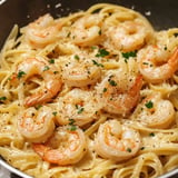 A close-up of creamy pasta with shrimp, garnished with parsley and black pepper.