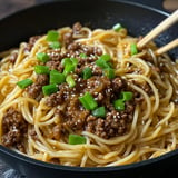 A close-up of a bowl of spaghetti topped with a meat sauce and garnished with chopped green onions and sesame seeds.