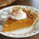 A slice of pumpkin pie topped with whipped cream and sprinkled with cinnamon on a decorative plate.