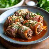 A plate of rolled beef stuffed with a savory filling, topped with herbs and breadcrumbs, served in a rich sauce.