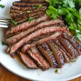 A plate of perfectly cooked, sliced steak garnished with fresh herbs.