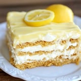 A slice of layered lemon dessert with creamy filling and a slice of lemon on top, served on a white plate.