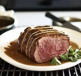 A perfectly cooked beef roast is served on a plate with a drizzle of sauce and garnished with fresh herbs.