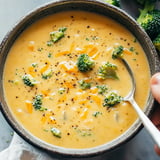 A bowl of creamy broccoli cheddar soup garnished with broccoli florets and shredded cheese.