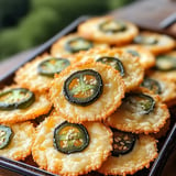 A close-up of cheesy, crispy snacks topped with sliced jalapeños and sesame seeds, presented on a tray.