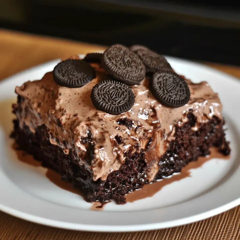 A chocolate cake topped with chocolate frosting and decorated with Oreo cookies is served on a white plate.